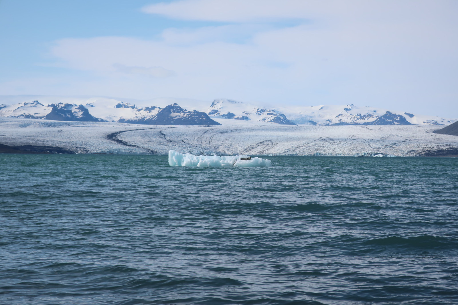 An iceberg floating before a glacier and snow-covered mountains in Iceland