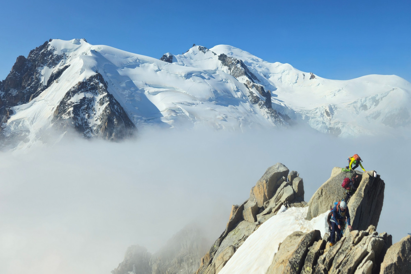 Three climbers moving across a rocky alpine ridge below Mont Blanc in France
