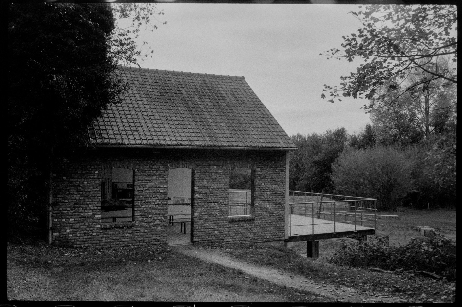 An open brick shelter and footbridge at the edge of woods in Heuvelland